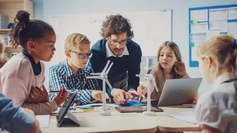 Profesor usa las TICs en la educación para enseñar a sus alumnos en un salón de clases con modelos a escala impulsados por computadoras