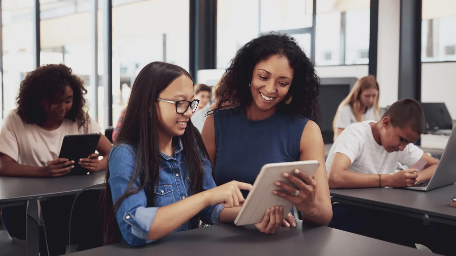 Egresada de la maestría en TIC para la educación enseña a una alumna a usar recursos digitales en un aula